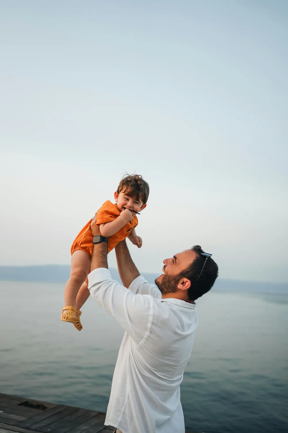 Padre levantando en brazos a su hijo pequeño junto al agua