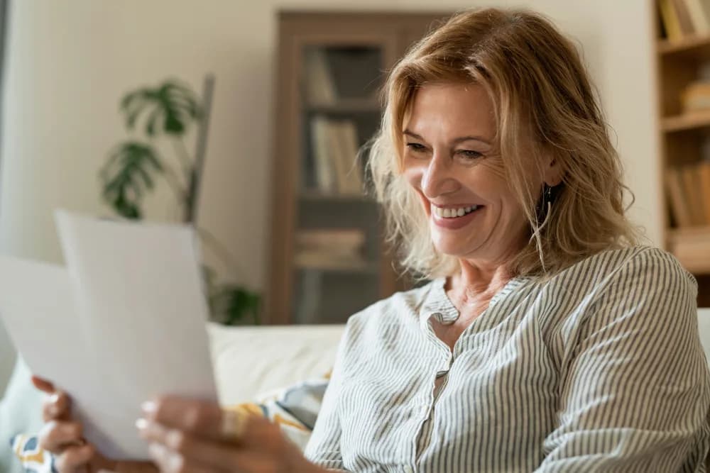 Mujer mayor leyendo una carta en el salón de casa, sonriendo